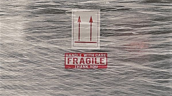 Package wrapped in plastic with label reading Handle With Care, Fragile, Thank You. Arrows indicate which side should be up.